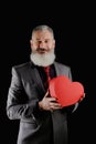 Mature bearded man wear suit holds red heart shaped gift box, isolated black background Royalty Free Stock Photo