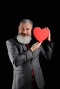 Mature bearded man wear suit holds red heart shaped gift box, isolated black background Royalty Free Stock Photo