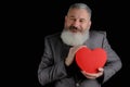 Mature bearded man wear suit holds red heart shaped gift box, isolated black background Royalty Free Stock Photo