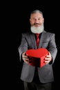 Mature bearded man wear suit holds red heart shaped gift box, isolated black background Royalty Free Stock Photo