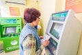 Mature beautiful woman pays utilities through the Sberbank ATM. Text in Russian: Sberbank, ATM