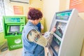 Mature beautiful woman pays utilities through the Sberbank ATM. Text in Russian: Sberbank, ATM