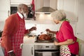 Mature black couple preparing Christmas dinner in their kitchen, man raising a glass as his wife bastes the roast turkey Royalty Free Stock Photo