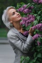 Mature blonde woman in gray suit walks in garden, admires flowers and smiles, selective focus