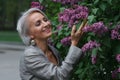 Mature blonde woman in gray suit walks in garden, admires flowers and smiles, selective focus