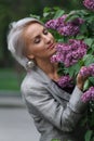 Mature blonde woman in gray suit walks in garden, admires flowers and smiles, selective focus