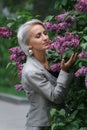 Mature blonde woman in gray suit walks in garden, admires flowers and smiles, selective focus