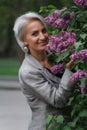 Mature blonde woman in gray suit walks in garden, admires flowers and smiles, selective focus