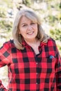 A mature blonde woman wearing a buffalo plaid flannel shirt red and black poses for a portrait in the Eastern Sierra Nevada