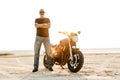 Mature bold man with tattoo looking at camera while posing by motorbike Royalty Free Stock Photo