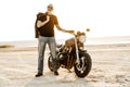 Mature bold man with tattoo looking at camera while posing by motorbike Royalty Free Stock Photo