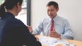 Mature boss senior Asian businessman leadership working together colleagues discuss information over a report document in a