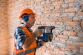 Mature builder in helmet using hammer drill