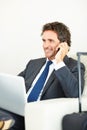 Mature business man ready for travel. Smiling executive sitting on a chair with laptop and talking on a cellphone. Royalty Free Stock Photo