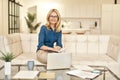 Mature business woman in casual wear smiling at camera, working from home while sitting on a couch in front of laptop in Royalty Free Stock Photo