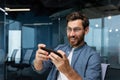 Mature businessman with beard is playing game on smartphone, man is having fun during break at workplace, businessman Royalty Free Stock Photo