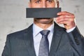 Mature businessman covering mouth with paper against white brick wall at office Royalty Free Stock Photo