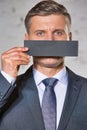 Mature businessman covering mouth with paper against white brick wall at office Royalty Free Stock Photo