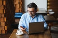 Mature businessman drinking coffee in cafe. Portrait of handsome man wearing stylish eyeglasses using laptop, looking at Royalty Free Stock Photo