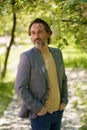 Mature businessman with grey beard wearing casual jacket and jeans spend time at park or garden looking thoughtful Royalty Free Stock Photo