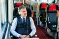 Mature businessman with headphones travelling by train. Royalty Free Stock Photo