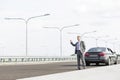 Mature businessman hitchhiking while standing with breakdown car on road Royalty Free Stock Photo