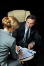 Mature businessman looking at blonde businesswoman signing papers Royalty Free Stock Photo