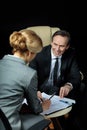 Mature businessman looking at blonde businesswoman signing papers Royalty Free Stock Photo