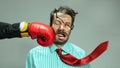 Mature man, businessman in red tie getting boxing punch in jaw from business competitors over grey background. Concept Royalty Free Stock Photo