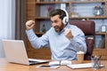 Mature businessman in shirt and headphones watching sports match at workplace inside office, man cheering having fun at Royalty Free Stock Photo