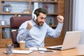 Mature businessman in shirt and headphones watching sports match at workplace inside office, man cheering having fun at Royalty Free Stock Photo