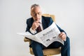 Mature businessman sitting in armchair and reading business newspaper isolated Royalty Free Stock Photo