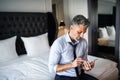 Mature businessman with smartphone in a hotel room.