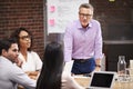 Mature Businessman Standing And Leading Office Meeting Of Colleagues Sitting Around Table Royalty Free Stock Photo