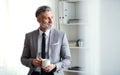 A mature businessman standing in an office, holding a cup of coffee. Copy space.