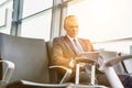 Mature businessman using digital tablet while sitting and waiting for boarding in his gate at airport Royalty Free Stock Photo