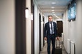 Mature businessman walking with luggage in a hotel corridor. Royalty Free Stock Photo