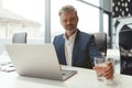 Mature businessman workingon laptop and drinking water while sitting in modern coworking