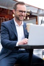 Mature Businessman Working On Laptop By Outdoor Coffee Shop Drinking Takeaway Coffee Royalty Free Stock Photo