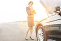 Mature businesswoman looking at breakdown car on road with yellow lens flare in background Royalty Free Stock Photo