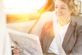 Mature businesswoman reading newspaper while sitting in car with yellow lens flare in background Royalty Free Stock Photo