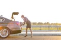 Mature businesswoman removing suitcase from car trunk on road against sky