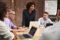 Mature Businesswoman Standing And Leading Office Meeting Around Table