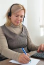 Mature businesswoman working using a calculator in a desk at office. She is using calculator and writing numbers down