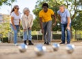 Metal petanque balls against four blurred multiracial senior players in the distance outdoors Royalty Free Stock Photo