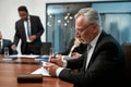 Mature caucasian businessman writing something in his note pad while having a meeting in the modern office Royalty Free Stock Photo