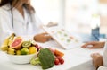 Mature caucasian doctor nutritionist in white coat recommends to young woman diet plan at table with organic vegetables Royalty Free Stock Photo