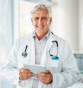 Mature caucasian male expert doctor smiling while using a digital tablet working at a hospital alone. One senior man Royalty Free Stock Photo