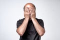 Mature caucasian man in black t-shirt covering his face with hands over gray background. Royalty Free Stock Photo