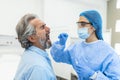 A mature Caucasian man in a clinical setting being swabbed by a healthcare worker in protective garb to determine if he has Royalty Free Stock Photo